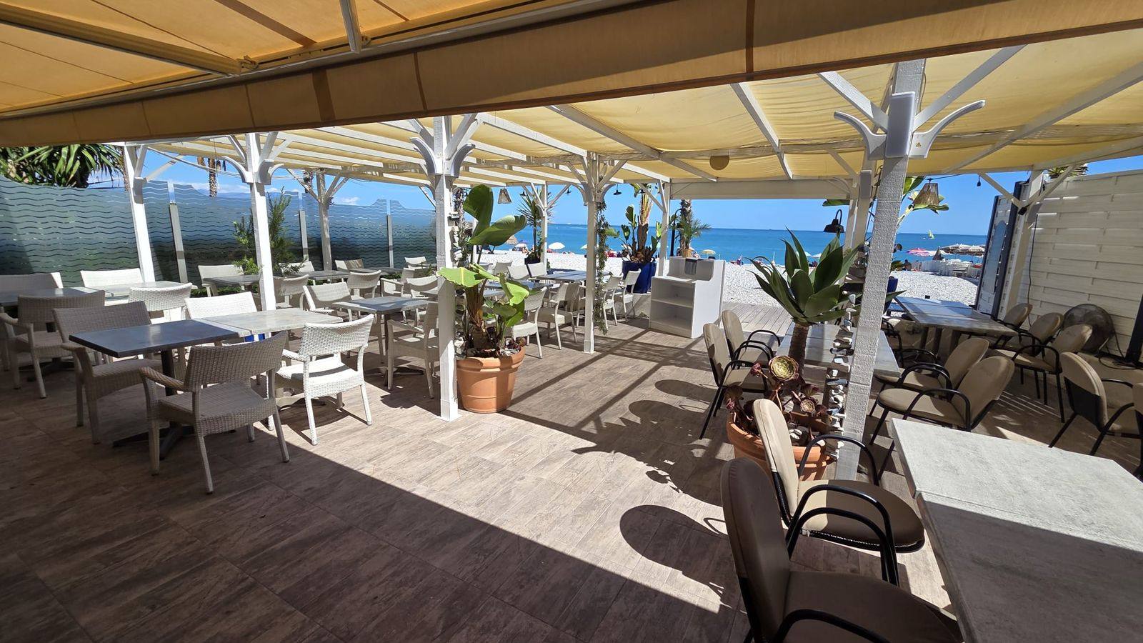 La grande terrasse ombragée de L&rsquo;Indigo, tables et fauteuils en osier tournés vers la plage